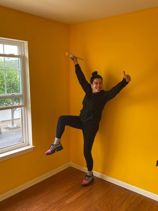 Michelle Rodriguez, founder of Flawless Management, celebrating in a freshly painted yellow bedroom